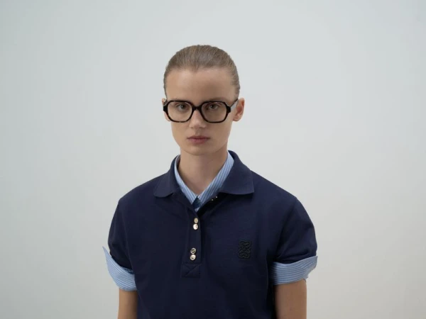 Model wearing dark glasses and a navy polo shirt against a plain white studio background