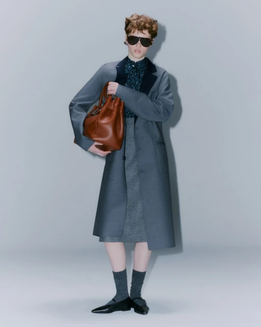 Fashionable woman in blue coat, sunglasses, and brown leather bucket bag, studio lit on neutral background, stylish and elegant.
