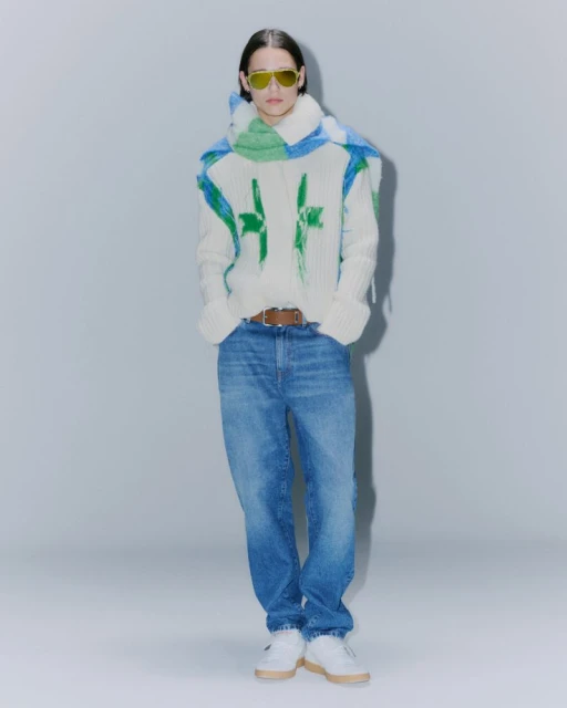 Fashionable adult in a painted sweater and blue jeans in a studio setting, showcasing style and modern design elements with a neutral backdrop.