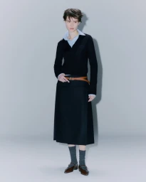 Model in black V-neck sweater and dark midi skirt with a brown belt against a plain grey background
