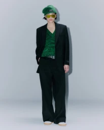 Model wearing a black blazer, green sweater, and green beanie against a grey seamless background.
