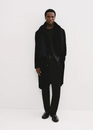 Model in dark coat and black scarf standing against a plain white background for Mango Winter Wardrobe.