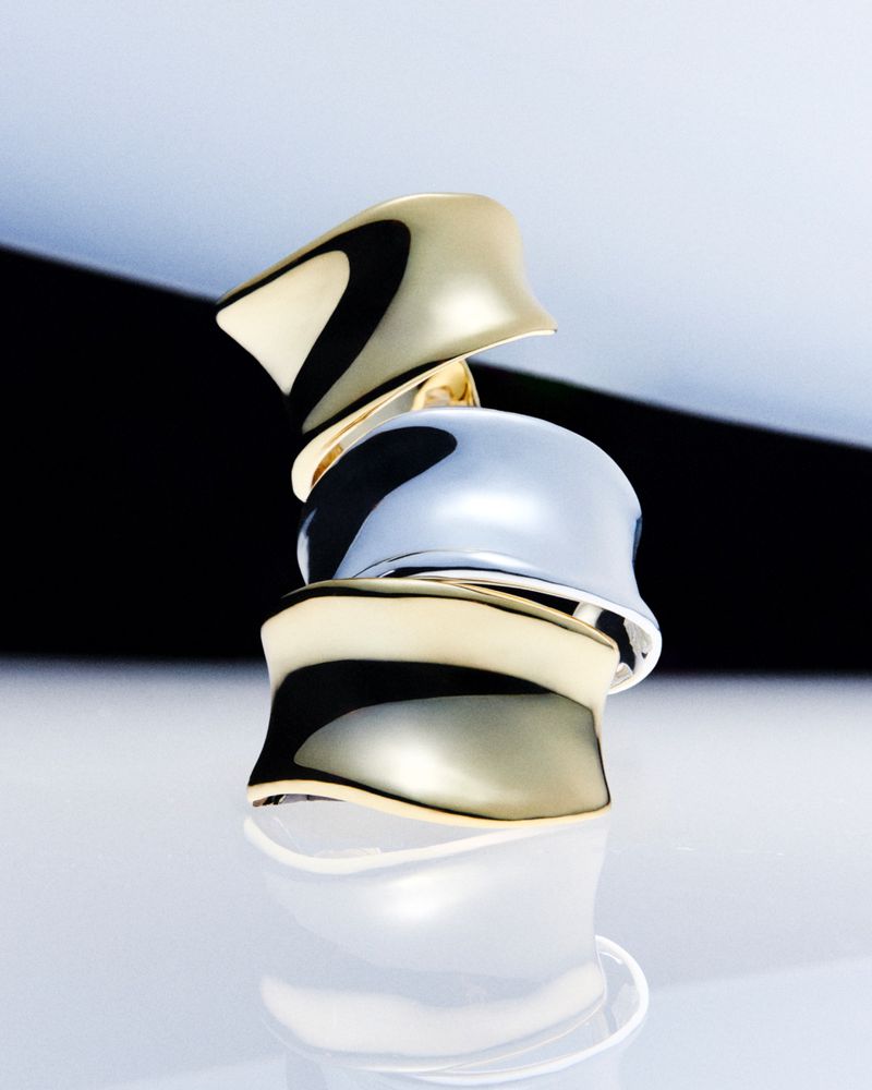 Stacked gold and silver rings with a glossy finish reflect light against a gradated black and white background, product photography.