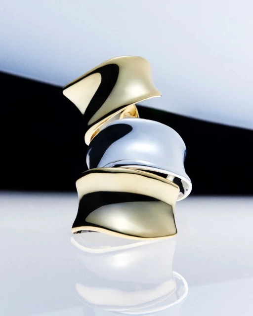 Stacked gold and silver rings with a glossy finish reflect light against a gradated black and white background, product photography.