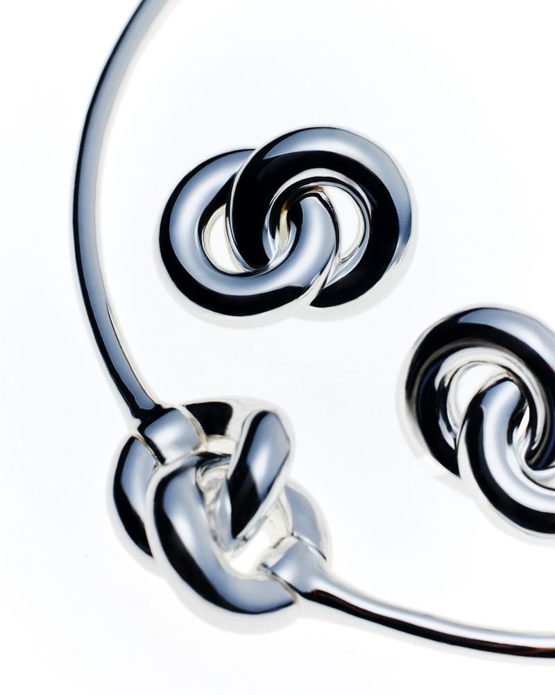 Silver choker necklace and matching earrings featuring a linked knot design, set against a clean white backdrop for jewelry product photography.