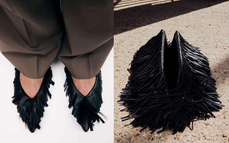 Eye-level shot of black fringed flats worn with brown trousers, and a fringed bag on a textured surface.