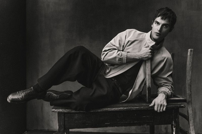 Parker Van Noord reclining on a wooden table with a chair in a monochrome fashion portrait for Zara.