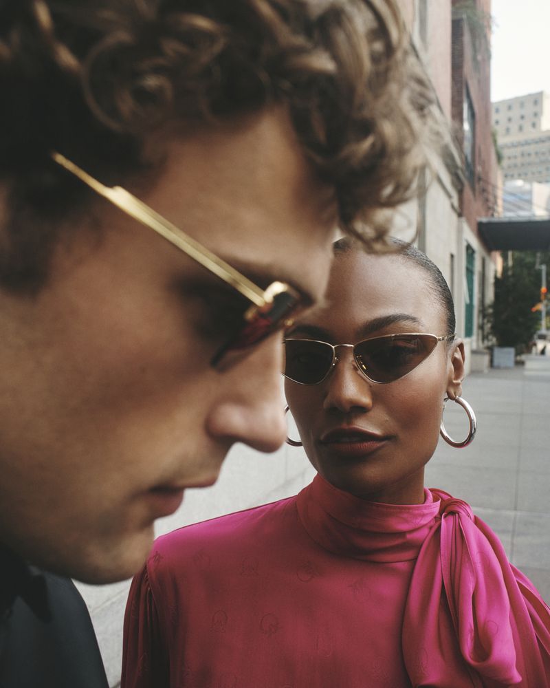Close-up portrait of two models wearing sunglasses outdoors on a city sidewalk for Saks OFF FIFTH FALL