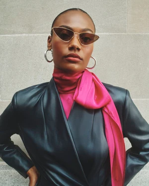 Model wearing a black leather jacket and vibrant pink silk scarf with large silver hoop earrings and cat-eye sunglasses.