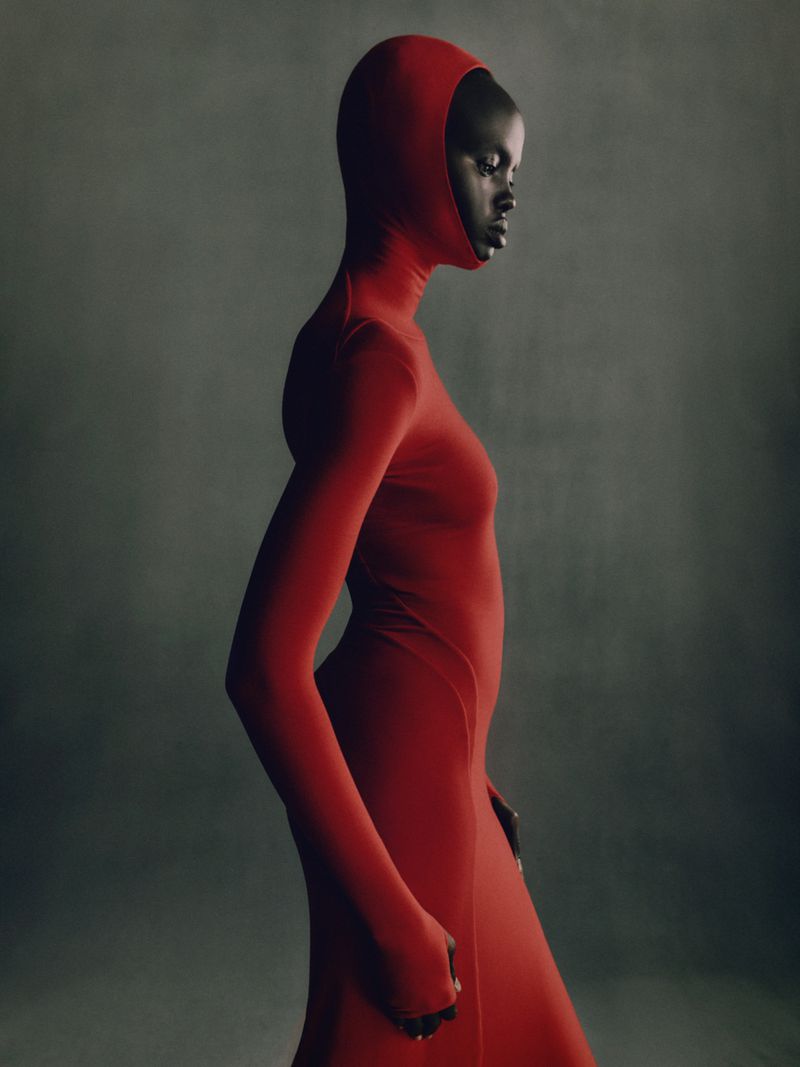 Elegant portrait of a Black woman in a full-body red hooded dress against a muted grey backdrop in a fashion editorial style image.