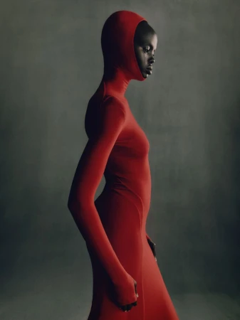 Elegant portrait of a Black woman in a full-body red hooded dress against a muted grey backdrop in a fashion editorial style image.