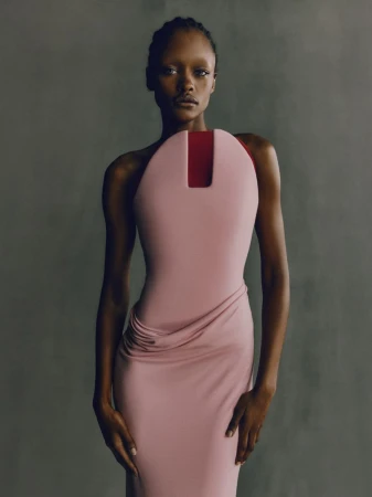 Fashionable African woman in a light pink dress posing in a studio. The dress features a unique square neckline and draped skirt.