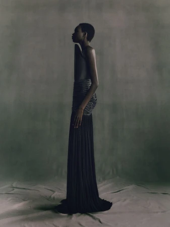 Striking studio portrait of an adult woman in an elegant black dress with intricate details, side profile, on a neutral-toned backdrop.