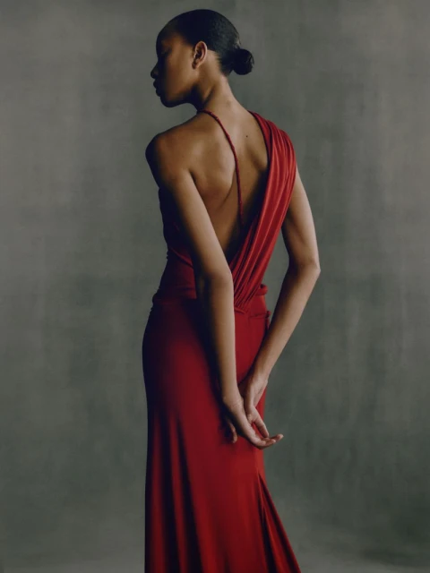 Elegant back view of an adult female in a long red gown, showcasing fashion and style against a neutral studio backdrop.