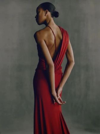 Elegant back view of an adult female in a long red gown, showcasing fashion and style against a neutral studio backdrop.