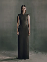 Model standing in a long dark green textured sleeveless dress against a neutral textured backdrop