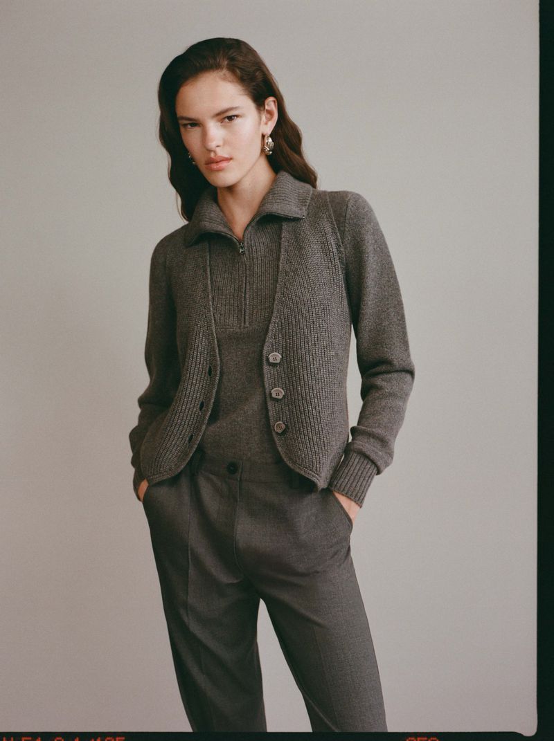 Portrait of woman in grey knit cardigan and trousers in a neutral studio. Classic, understated style, warm lighting and natural pose.