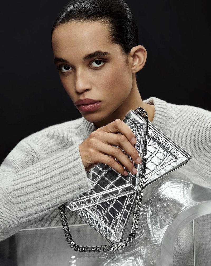 Model Lara Menezes holding a silver metallic handbag wearing a grey knit sweater in Michael Kors Collection SS 2025 campaign.
