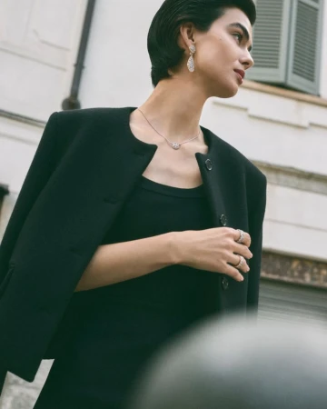 Portrait of an adult female in a black dress with a black jacket, posing outdoors with a silver necklace and earrings.