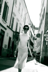 Model in white turtleneck dress walking down a city street with tall buildings