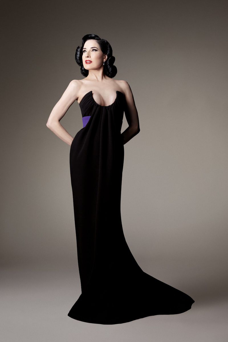Portrait of elegant woman in long black dress with train posing in studio, looking up. Red lipstick and classic hairstyle. Formal fashion.