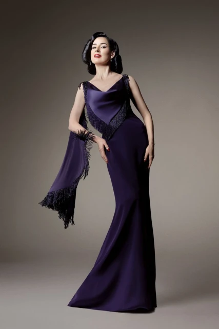 Elegant adult woman poses in a purple gown with fringed shawl in a studio setting, showcasing classic beauty and high-fashion style.