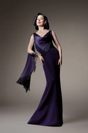 Elegant adult woman poses in a purple gown with fringed shawl in a studio setting, showcasing classic beauty and high-fashion style.