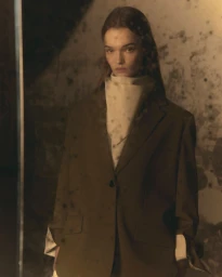 Model wearing an oversized brown blazer and patterned neck scarf against a textured backdrop for Ami Fall-Winter 25.
