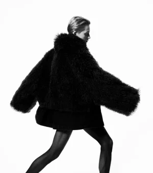 Model in voluminous black furry jacket posing dynamically against a stark white studio background