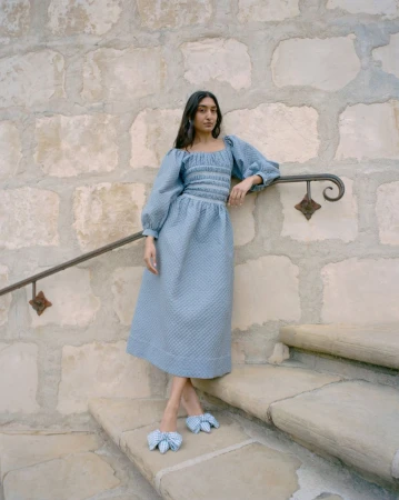 Model Lizzy Yusuff in a textured blue dress leaning against a stone staircase for Loeffler Randall FW24