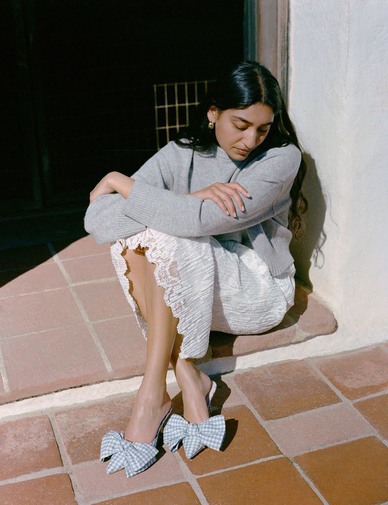 Model Lizzy Yusuff wearing a grey sweater and white lace skirt with bow mules for Loeffler Randall FW24.