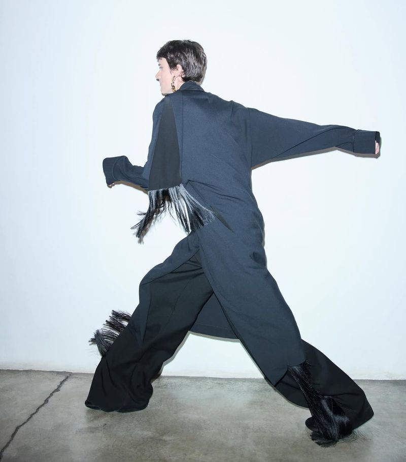 Woman in dark wide-leg pants and an oversized top strikes a dynamic pose against a bright white background, showcasing a fashion-forward look.