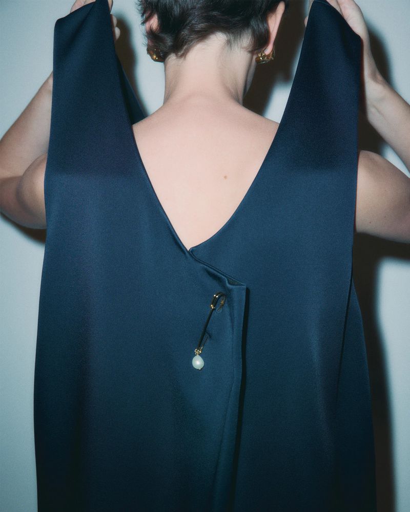Back view of a female adult wearing a dark blue dress with a pearl brooch. Close-up studio shot with shallow depth of field.