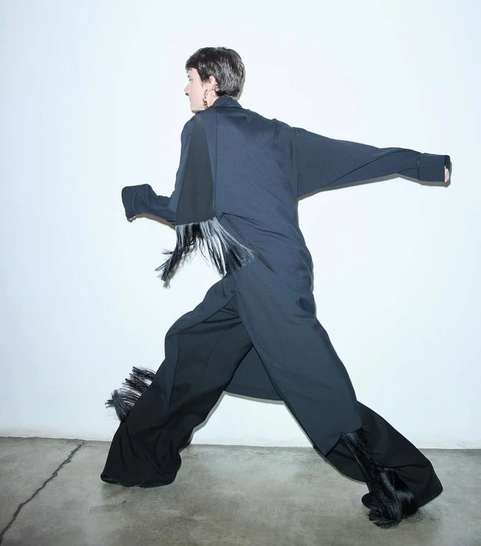 Model in dark coat and trousers striding across a minimalist white studio background captured by Bibi Cornejo Borthwick