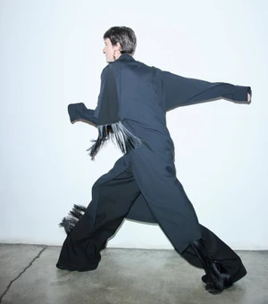 Model in dark coat and trousers striding across a minimalist white studio background captured by Bibi Cornejo Borthwick