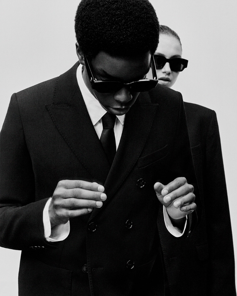 Monochrome fashion portrait of a man and woman in black suits and sunglasses for Ami SS24 eyewear campaign.