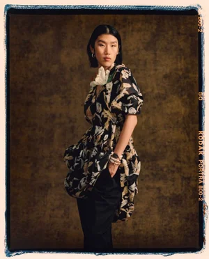 Model Jiashan Liu wearing a floral print dress and black trousers against a textured background for 3.1 Phillip Lim.