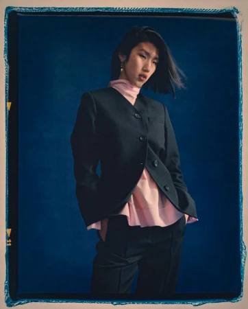 Model Jiashan Liu wearing a dark blazer over a pink top against a textured blue background for 3.1 Phillip Lim.