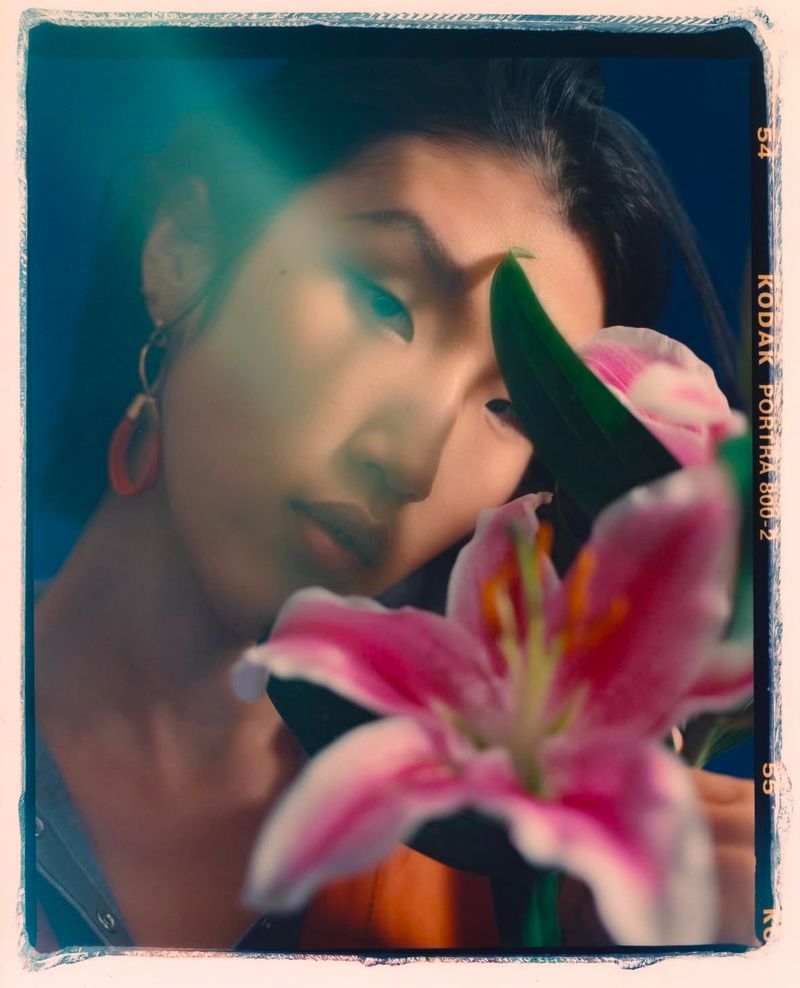 Portrait of a young Asian woman with flowers, framed by film border, featuring soft lighting and pink floral accents against a blue backdrop.