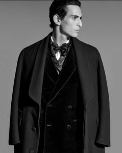Model wearing a black velvet coat and bow tie against a solid grey background for Dunhill AW24 lookbook