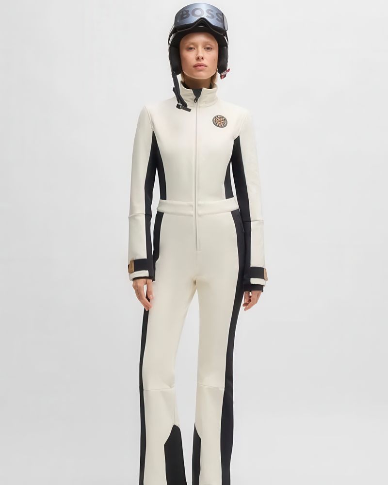 Full shot of a model in a white and black ski suit and a helmet with goggles in a white photo studio. Fashion photography.