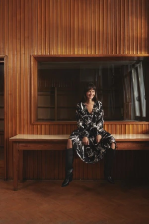 Model Marta Dyks sitting on a wooden counter wearing a black and white patterned dress and knee-high boots