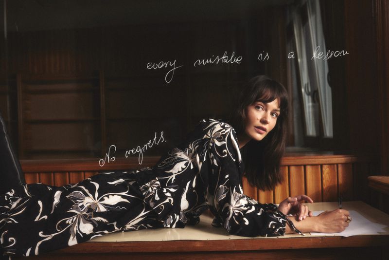 Adult female model in floral top poses on a brown table surface with the handwritten phrase 'every mistake is a lesson'.