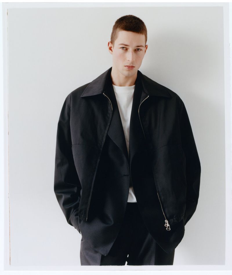 Portrait of a male model wearing a black jacket and white t-shirt against a plain white studio background.