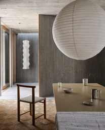Large spherical white paper lantern hanging over a wooden dining table in a modern interior with concrete walls