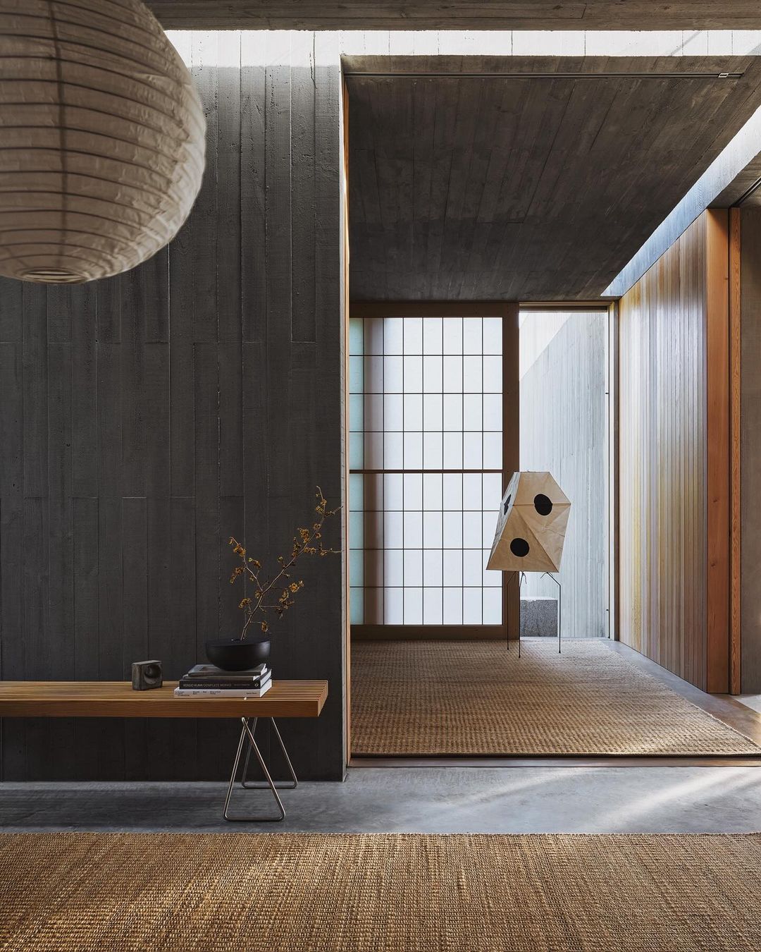 Minimalist interior with wooden bench, paper lantern, and geometric sculpture in neutral tones. Modern architectural design, concrete and wood elements.