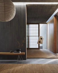 Modern interior with woven jute rugs on the floor, a wooden bench with books and a vase, and a large round paper lantern hanging above.