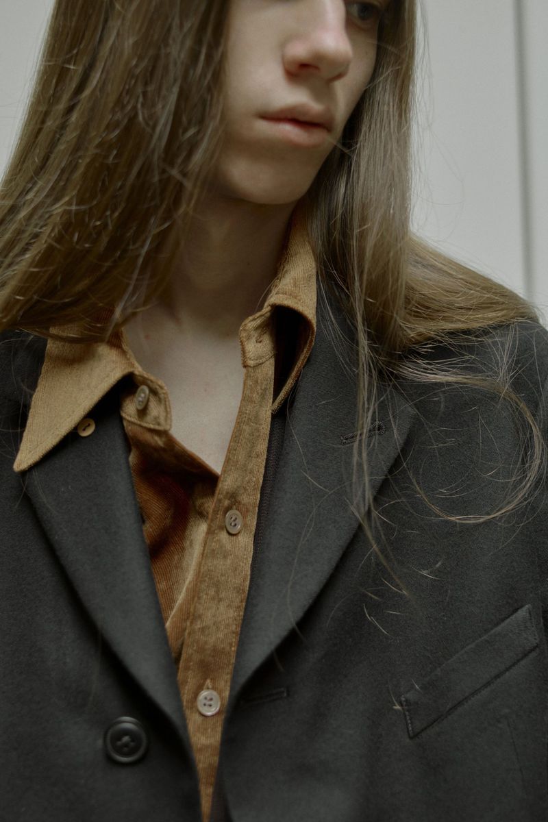 Close-up of a person with long brown hair wearing a black blazer and a brown button-down shirt, showcasing fashion and style.