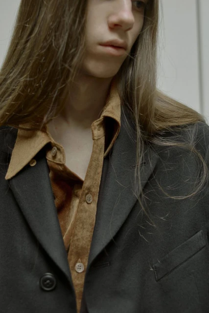 Close-up of a person with long brown hair wearing a black blazer and a brown button-down shirt, showcasing fashion and style.