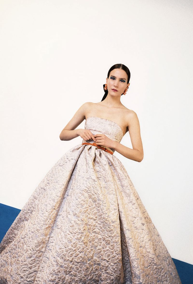 A woman wearing a formal strapless dress with a full skirt poses against a stark background, showcasing a modern take on classic elegance.